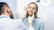 Ein Dermatologe untersucht die Haut der Augenpartie einer Patientin.